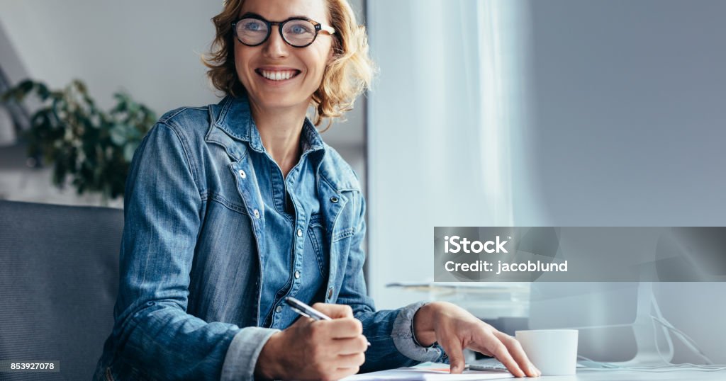 Caucasian woman working at her desk in office Caucasian woman working at her desk in office. Female executive looking away and smiling. Looking Away Stock Photo