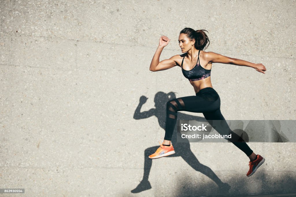 Fit young woman jumping and running Young woman with fit body jumping and running against grey background. Female model in sportswear exercising outdoors. Women Stock Photo