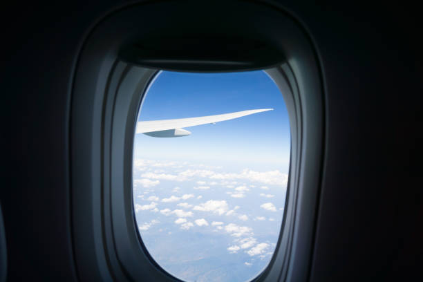 istock Outlook through plane window while traveling with window surround framing blue sky and clouds with focus on wing outside. 853930622