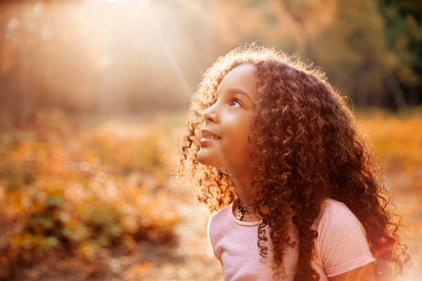 afro american cute little girl with curly hair receives miracle sun rays from the sky - praying girl imagens e fotografias de stock