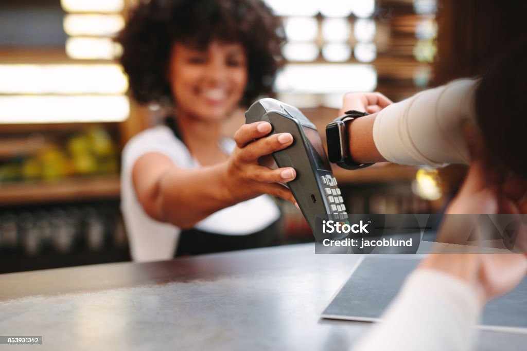 Customer paying bill using a smartwatch Customer making wireless or contactless payment using smartwatch. Store worker accepting payment over nfc technology. Paying Stock Photo