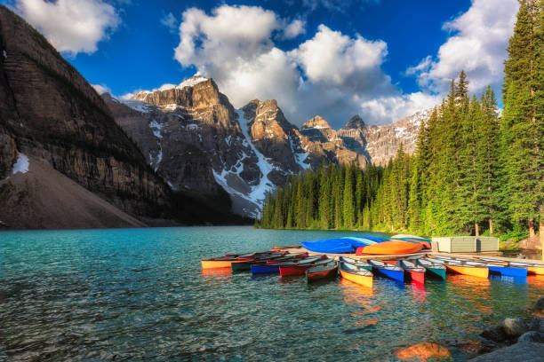 Canoes on Moraine lake in Banff national park, Canada Canoes on beautiful turquoise waters of the Moraine lake an sunrise with snow-covered peaks above it in Banff National Park of Canada moraine lake stock pictures, royalty-free photos & images