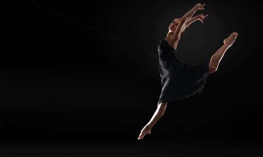 Young beautiful professional  ballet dancer over black background