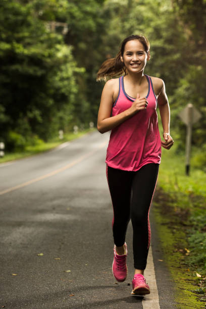 donna asiatica stava facendo jogging sulla strada nella foresta con tempo soleggiato - running jogging asian ethnicity women foto e immagini stock