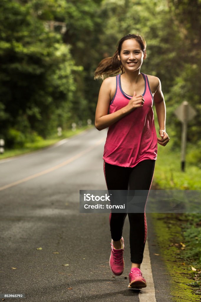 Asian woman were jogging on the road In the forest with sunny weather Running Stock Photo