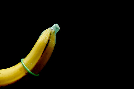 Yellow banana fruit with condom wear An example of how to use a condom correctly. For teaching or advertising media. Prevent unintentional black background. copy space.