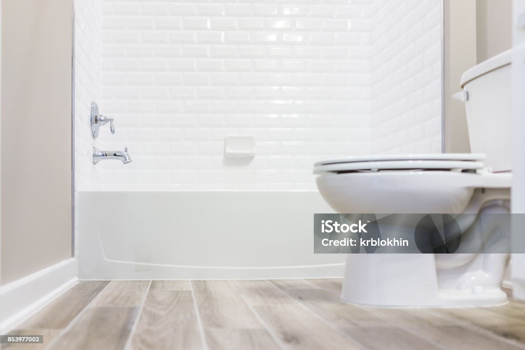 Modern white plain clean toilet bathroom with shower tiles and hardwood floors from ground level Toilet Stock Photo