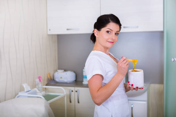 Beautician wearing black gloves checking green hot wax with wooden spatula before depilation treatment