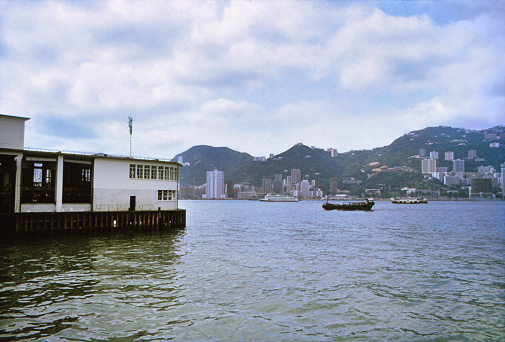 Historic photo of the British Colonial Hong Kong, 1989. The view of the city skyline of the island of Hong Kong, the Victoria Harbor from the Star Ferry Terminal in the Kowloon peninsula.
