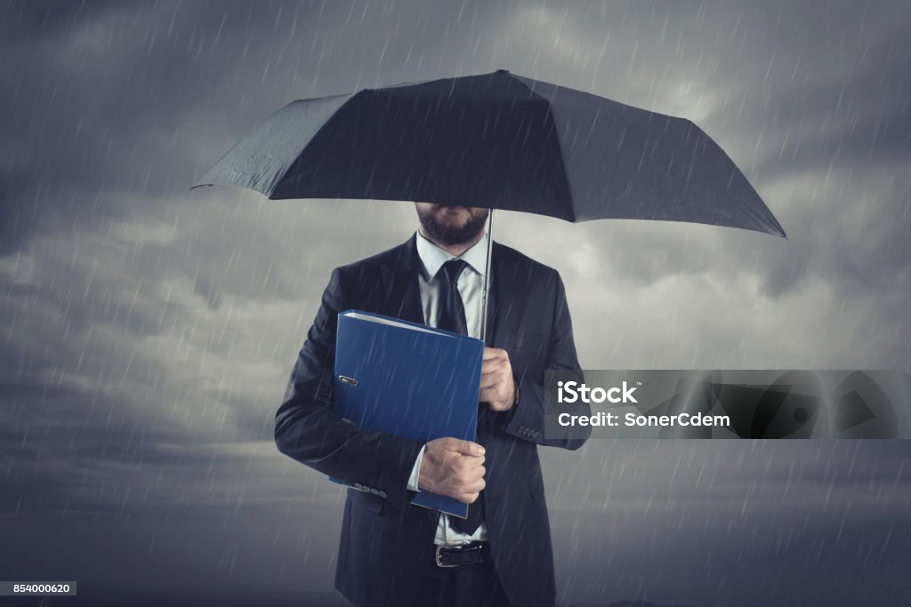 Businessmen with umbrella standing in stormy rain.Insurance agent and consultant in business crisis situation. Insurance Stock Photo