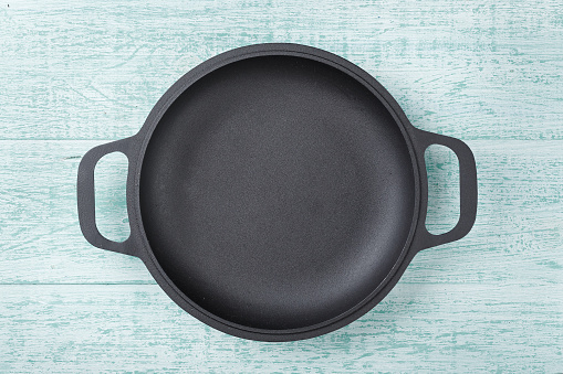 A small cast-iron frying pan for cooking for one person, a frying pan on a light wooden background