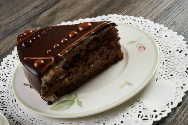 Delicious chocolate cake with chocolate cream and nuts on plate. Slice of chocolate cake and cup of tea on wooden table background