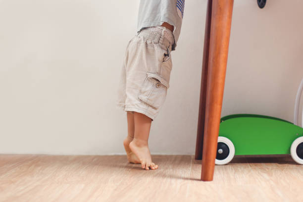 Closeup photo of Asian 18 months / 1 year old toddler baby boy child standing on tiptoes floor at home stock photo