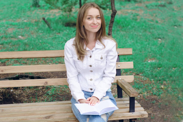 istock Beautiful young woman on a nature bench reading a book 854044620