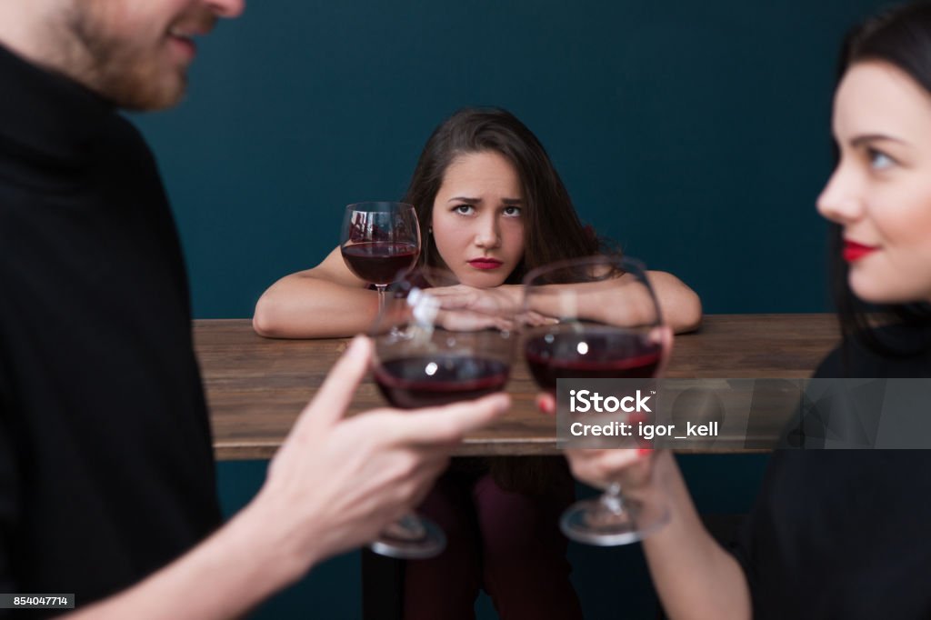 Sad alone female in bar. Jealousy backdrop Sad alone female in bar. Jealousy backdrop. Love triangle, cheating relationships. Unhappy betrayed woman in focus on blue background, loneliness concept Envy Stock Photo