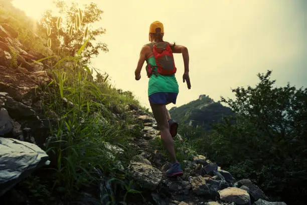 Photo of young woman trail runner running at great wall on the top of mountain