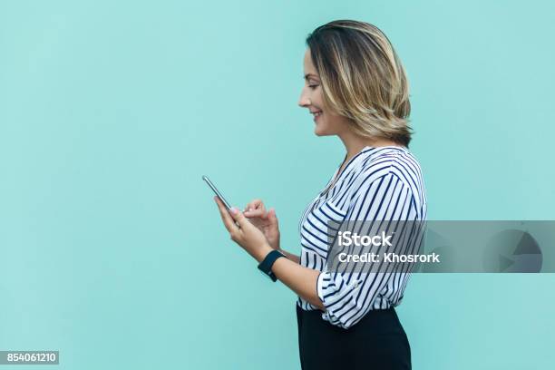 Side View Of Happiness Business Woman Punished Alone At Blue Wall And Using Smartphone Stock Photo - Download Image Now