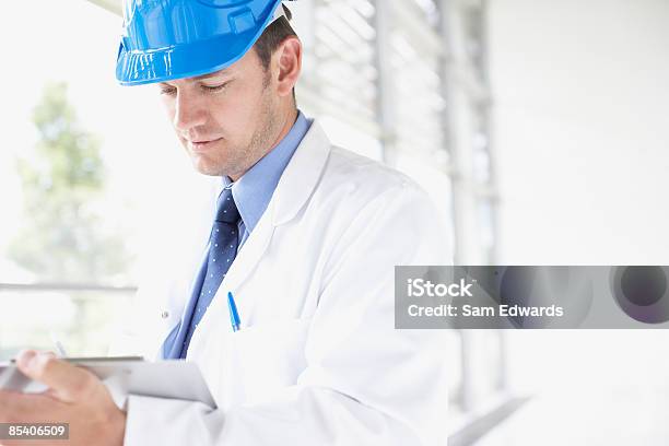 Businessman In Hardhat Writing On Clipboard Stock Photo - Download Image Now - Hardhat, Lab Coat, 30-34 Years