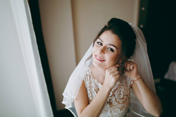 istock Beautiful bride puts on earrings at the window 854079000