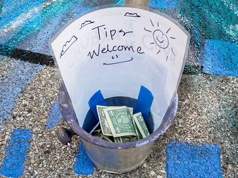 A metal can with a sign saying tips are welcomed.  People have dropped American dollars in the tip can.