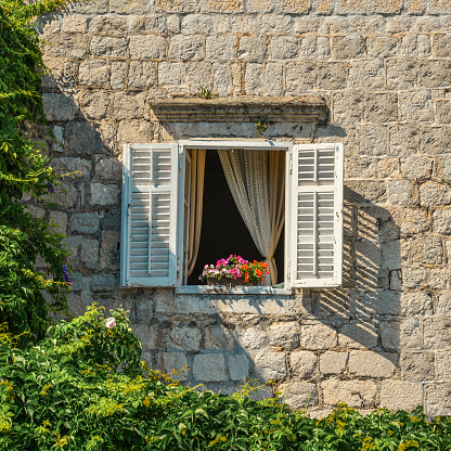 A typical montenegrian window with louvered shuters and  flowers in hanging flower pots