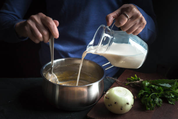 Milk from the jug is poured into a base sauce for making bechamel stock photo