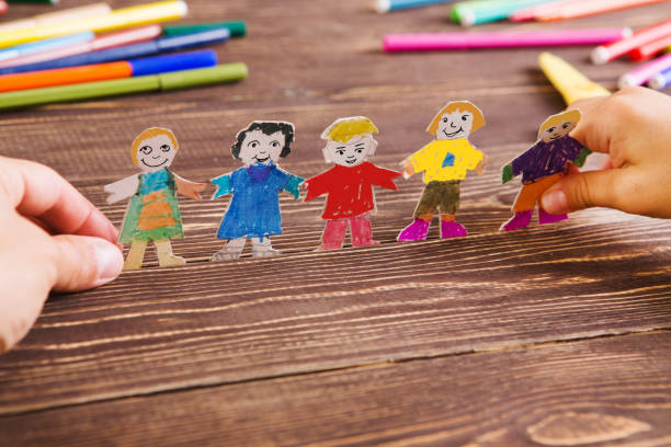 el niño hace figuras de personas de papel. personas de papel sobre fondo de madera. juego de niños creativos con el arte. - primary colours fotografías e imágenes de stock