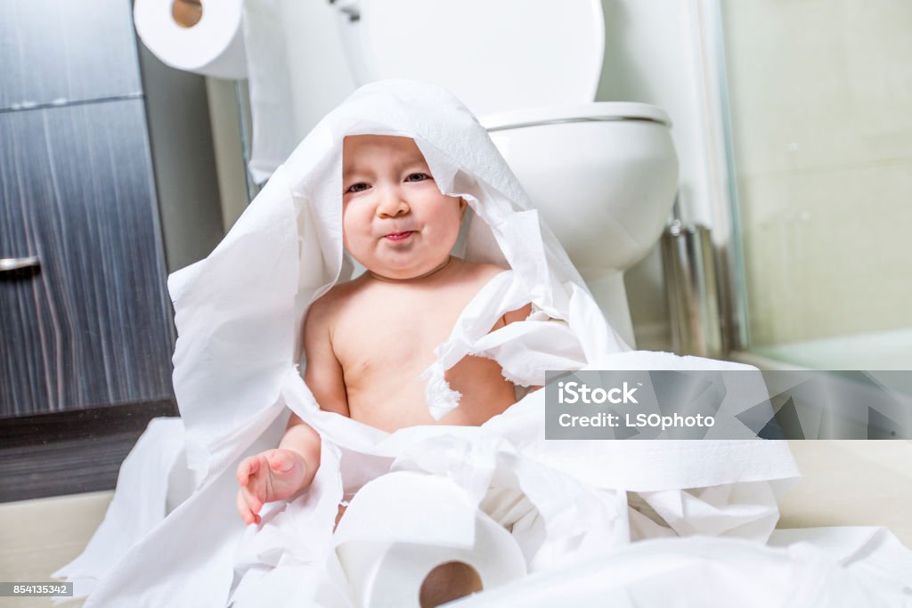 Toddler ripping up toilet paper in bathroom A Toddler ripping up toilet paper in bathroom Messy Stock Photo