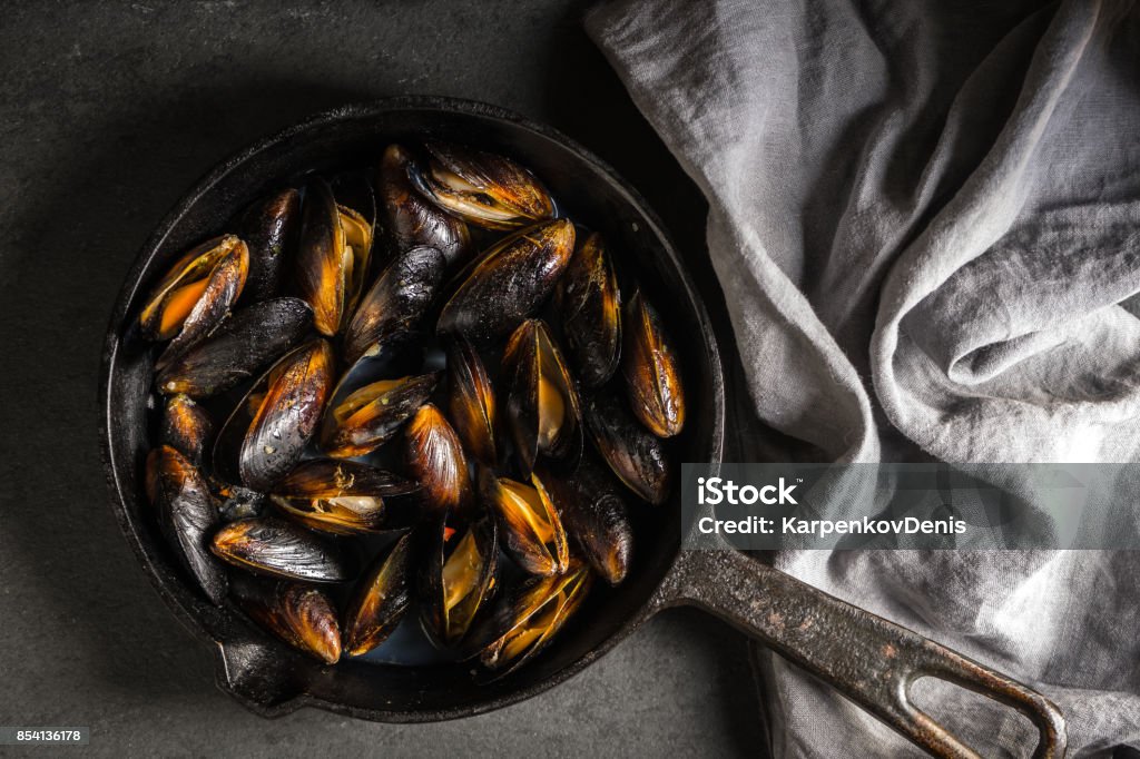 Mussels on a cast-iron frying pan and napkin on a gray background diagonal Mussels on a cast-iron frying pan and napkin on a gray background diagonal horizontal Backgrounds Stock Photo