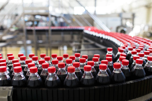 Juice and soda production factory Bottling factory - Black juice or soft drink bottling line for processing and bottling juice into bottles. Selective focus. bottling plant stock pictures, royalty-free photos & images