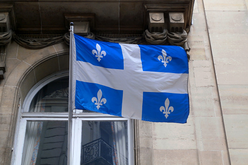 Flag of the Québec waving in front of the facade of a building.