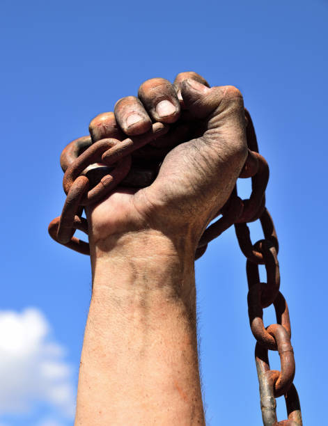 mano del hombre envuelto en una cadena de hierro oxidado levantado contra un cielo azul - arms lifted fotografías e imágenes de stock