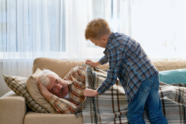 Careful grandson covering grandpa with blanket Loving grandson taking care of grandfather and covering his with blanket when he sleeping on sofa in living room sleeping grandpa stock pictures, royalty-free photos & images