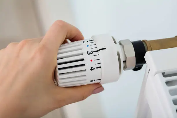 Close-up Of Woman's Hand Adjusting Radiator Thermostat Valve At Home