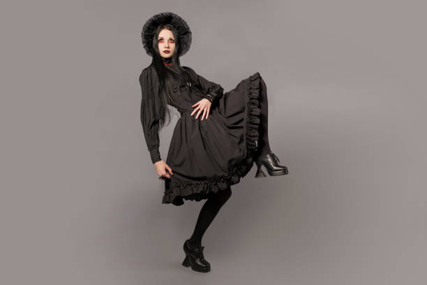 ritratto di donna bruna in abito nero e classico stile gotico con occhi rossi su sfondo grigio. concetto di halloween. - goth foto e immagini stock