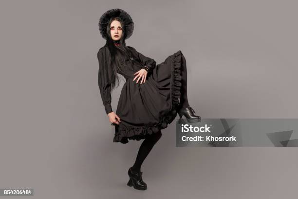 Portrait Of Brunette Woman In Black Dress And Classic Gothic Style With Red Eyes On Gray Background Halloween Concept Stock Photo - Download Image Now