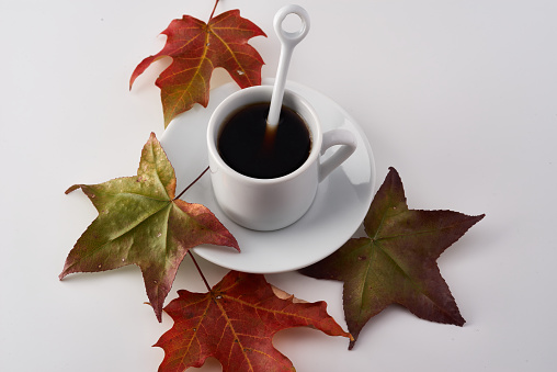 Autumn seasonal décor. Black roasted coffee beans. Colorful autumn leaves. Decoration pumpkins, baskets and orange color plate. Black coffee in white cup.