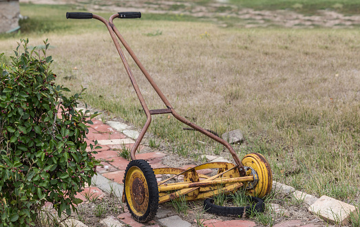 horizontal image of an old vintage antique manual push mower with a broken wheel.