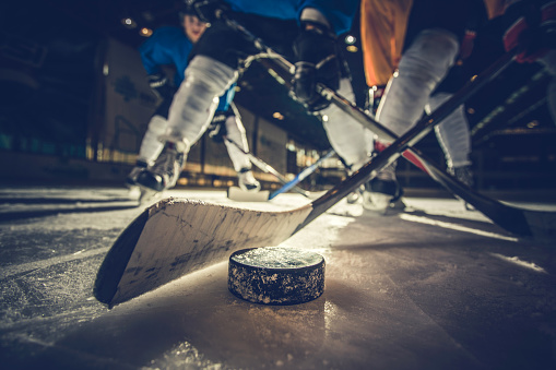 Close up of hockey puck and stick during a match with players in the background.