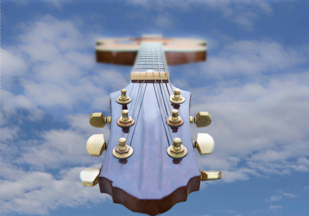 Looking down an accoustic guitar head and neck to the blue sky . There is space for text on each side of the image which gives the impression that the guitar is floating in the sky. Retro type image from the 80's