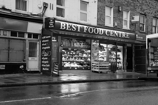 Typical neighborhood food and grocery shop on Roman Road in East London's suburb of Bow on a wet day in monochrome.