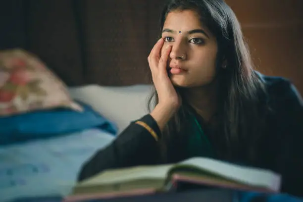 Education: Indoor image of Asian, Indian serene young woman studying and thinking at home. One person, waist up and selective focus with copy space.
