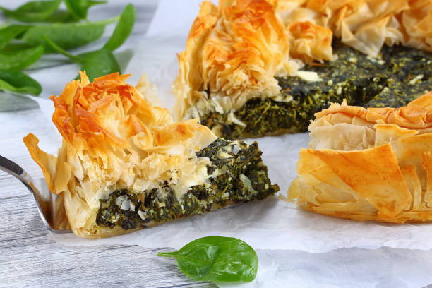 golden crust hot greek spinach pie delicious golden crust hot greek spinach feta cheese pie or spanakopita cut in slices on white paper with spatula on table, authentic recipe, side view from above, close-up spanakopita stock pictures, royalty-free photos & images