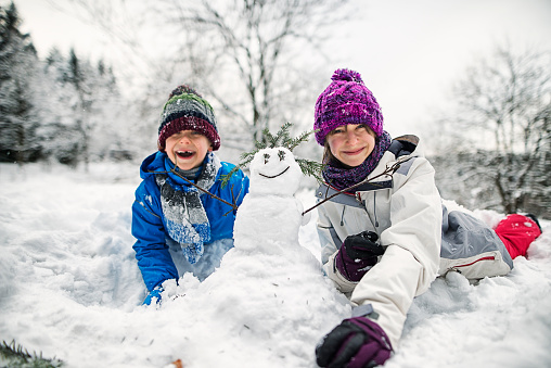Cold winter day. Little boy and little girl went outside to play with snow. They are building a small cute snowman. Kids are aged 11 and 7.