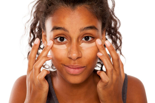 een donkere gevilde jongedame geldt een concealer onder de ogen met haar vingers - tipp ex stockfoto's en -beelden