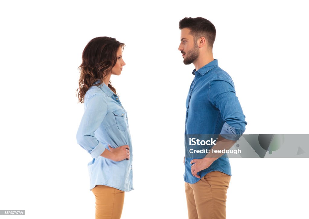 serious casual couple with hands on waist facing each other face to face serious casual couple with hands on waist, on white background Face To Face Stock Photo