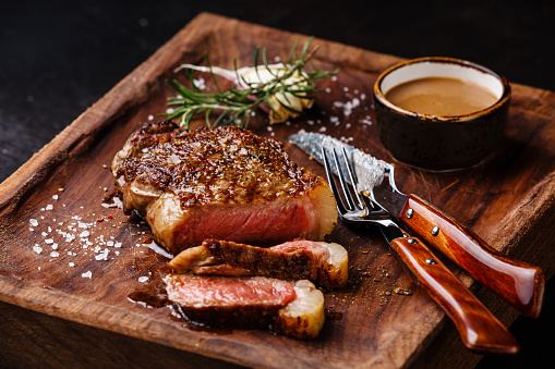 Sliced grilled meat steak New York Striploin with Pepper sauce and knife and fork on wooden board on black background