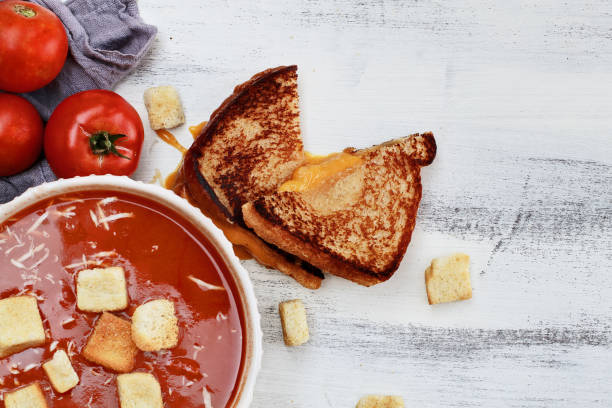 Hot tomato soup with Parmesan cheese and croutons served with a grilled cheese sandwich. Image shot from above in flat lay style.