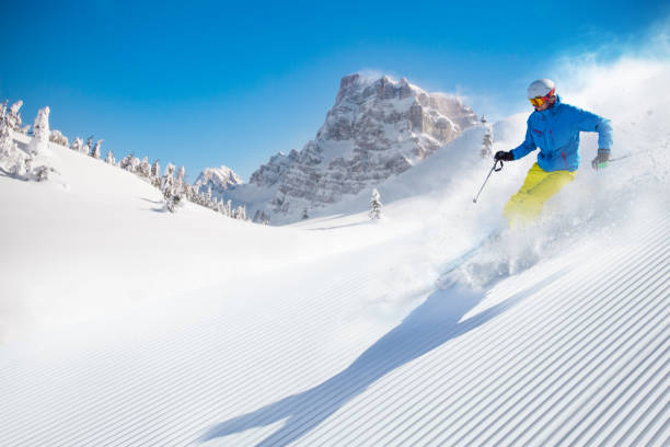 Skier skiing downhill in high mountains during sunny day.