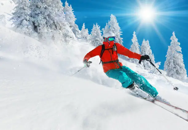 Skier skiing downhill in high mountains during sunny day.